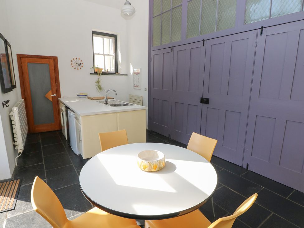 A kitchen with a round white table and orange chairs a sink and counter along one wall and large purple paneled doors at Zoar Chapel in Carew