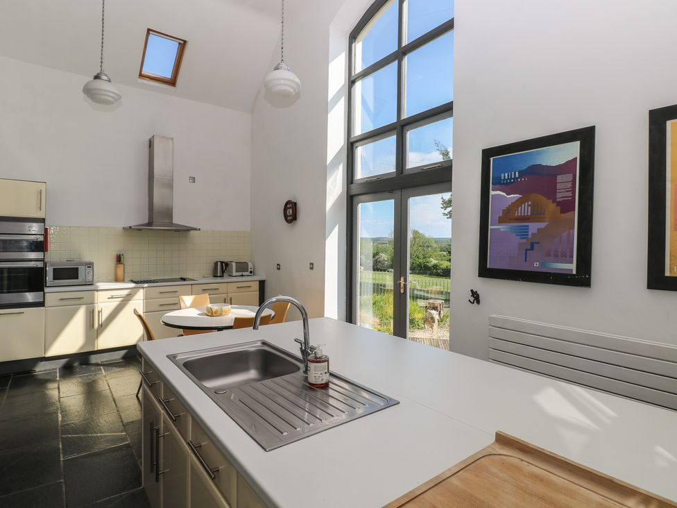 A kitchen with a sink on an island and a round dining table near large windows at Zoar Chapel in Carew