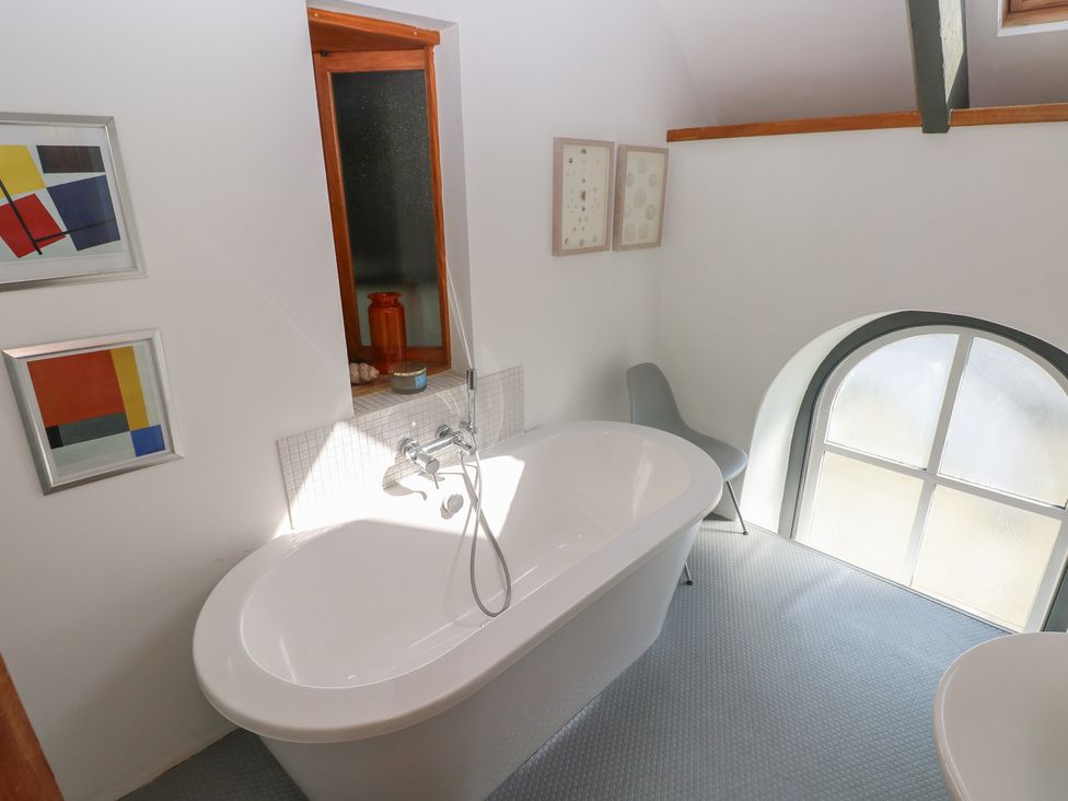 A bathroom with a freestanding bathtub a chair two framed pictures and a window at Zoar Chapel in Carew