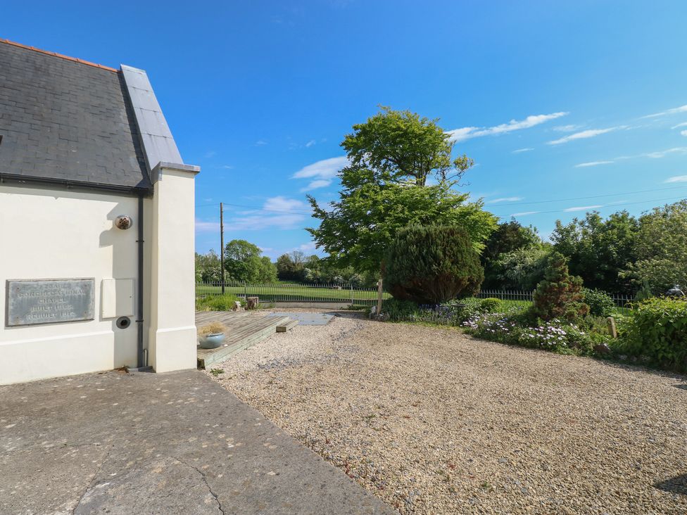 An outdoor area with a gravel driveway green bushes and trees next to a white building under a blue sky at Zoar Chapel in Carew