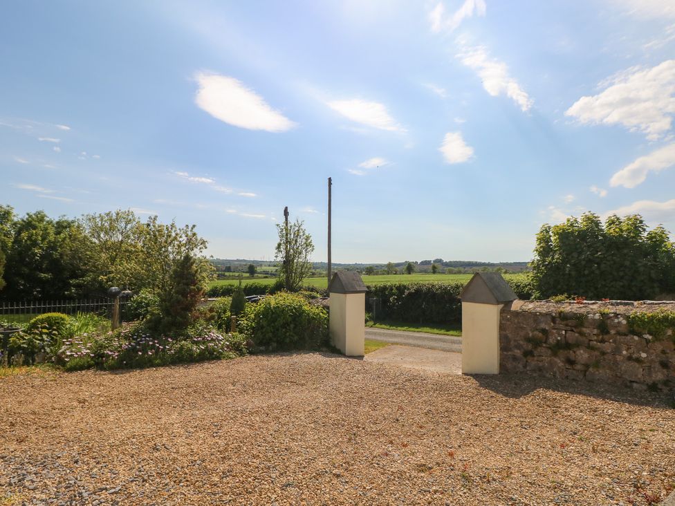 A gravel driveway with garden beds and an open gate leading to a road and fields at Zoar Chapel in Carew