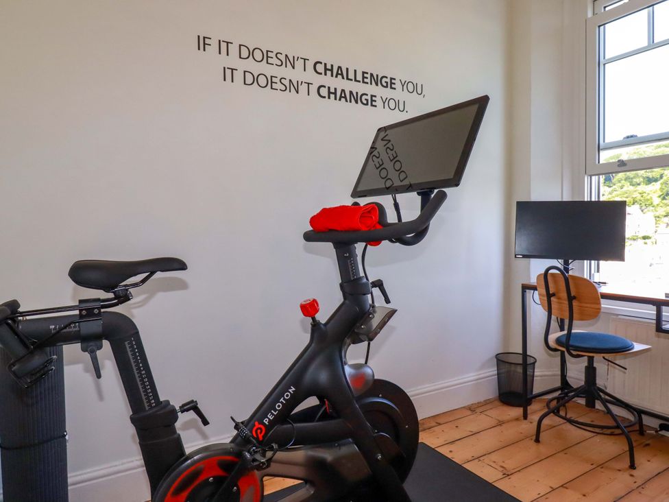 A home gym with a Peloton bike and a desk with a monitor at Harbour House in Looe