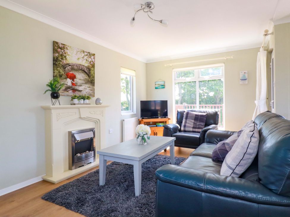 A living room with a fireplace a gray coffee table black leather sofas and a TV at Lodge 9- Lamorna Tregolds near St Merryn