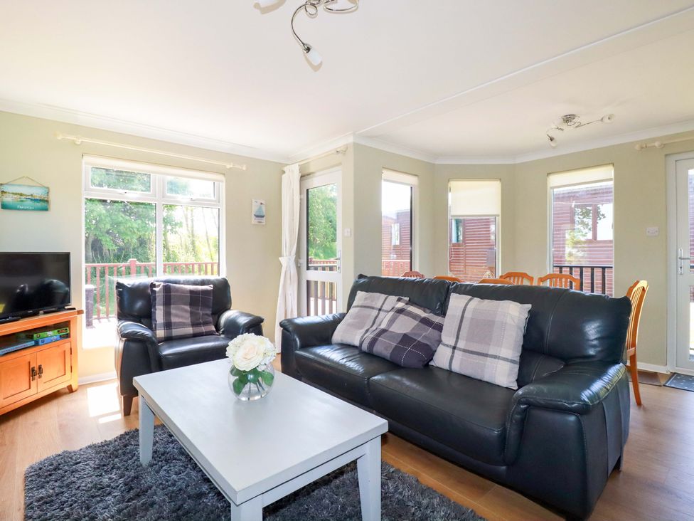 A living room with black leather sofas a white coffee table and a dining area at Lodge 9- Lamorna Tregolds near St Merryn