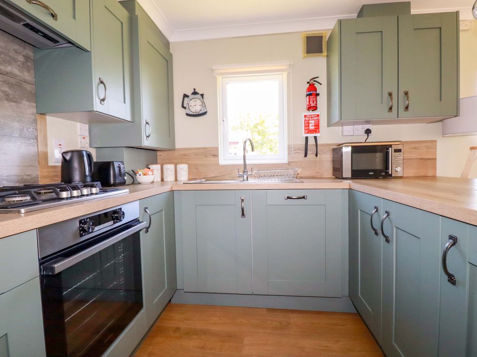 A kitchen with green cabinets a gas stove oven microwave kettle toaster sink and countertop at Lodge 9- Lamorna Tregolds near St Merryn