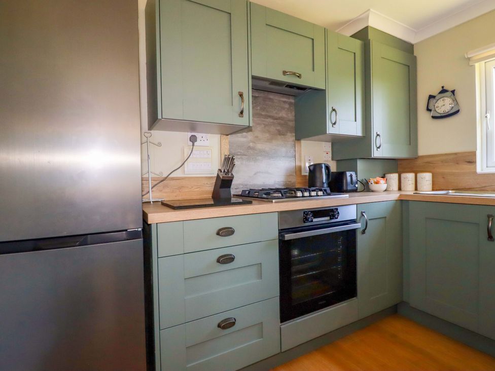A kitchen with green cabinets a stainless steel refrigerator a gas stove an oven a kettle a toaster and containers on the countertop at Lodge 9- Lamorna Tregolds near St Merryn