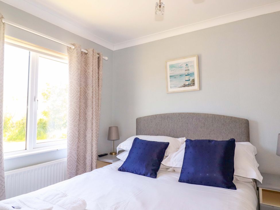 A bedroom with a bed with blue pillows bedside tables with lamps and a window with curtains at Lodge 9- Lamorna in Tregolds near St Merryn