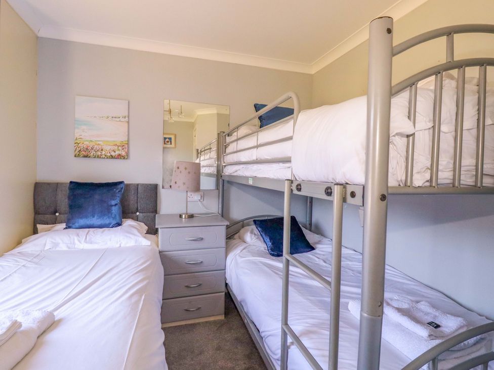 A bedroom with a single bed and a bunk bed with blue pillows and a bedside table with a lamp at Lodge 9- Lamorna in Tregolds near St Merryn