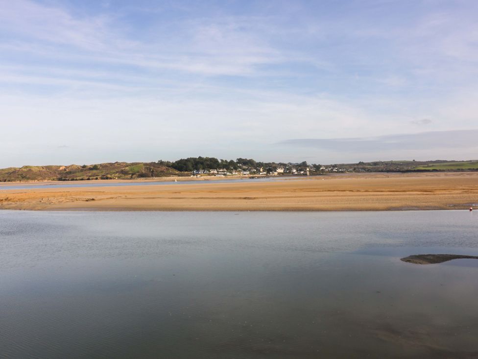 A view of a river with sandy banks and a village with houses and trees in the background at Lodge 9- Lamorna in Tregolds near St Merryn