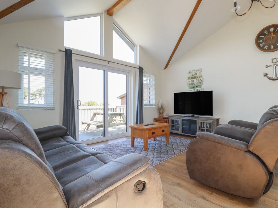 A living room with brown sofas a wooden coffee table a television and sliding glass doors leading to an outdoor picnic table at Lodge 18 in St Merryn