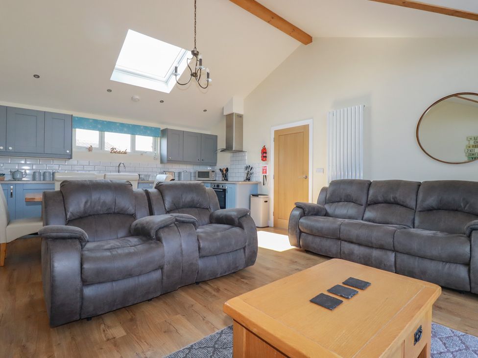 A living room with grey sofas a wooden coffee table and a kitchen with blue cabinets at Lodge 18 in St Merryn