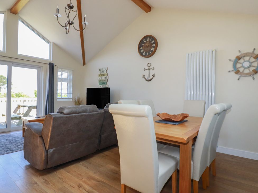A dining table with six chairs and a living room with a sofa near glass doors at Lodge 18 in St Merryn