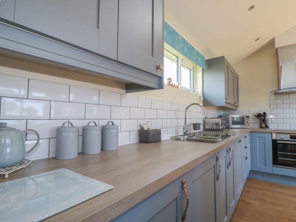 A kitchen with blue cabinets white tiled backsplash and wooden countertop at Lodge 18 in St Merryn