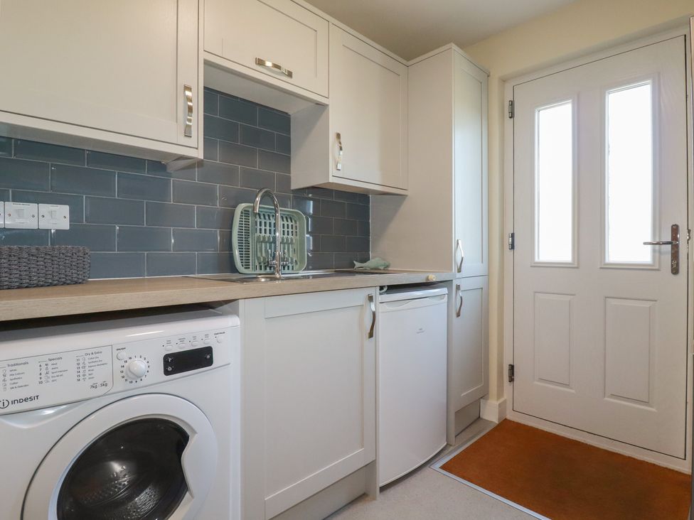 A laundry room with a washing machine a sink white cabinets and a door at Lodge 18 in St Merryn