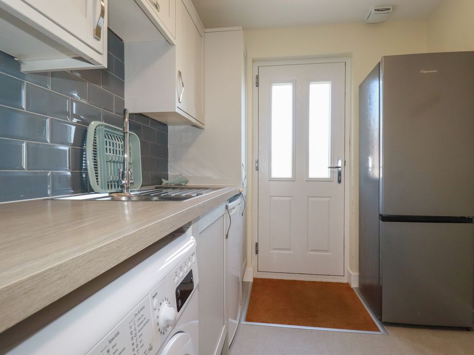 A kitchen with a washing machine under the counter a stainless steel sink a drying rack a refrigerator and a white door with windows at Lodge 18 in St Merryn