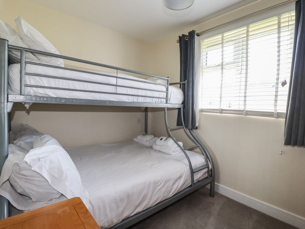 A bedroom with a metal bunk bed and window with blinds and curtains at Lodge 18 in St Merryn