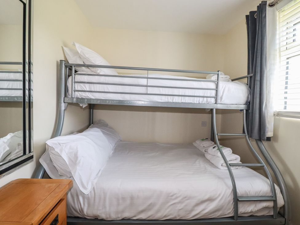 A bedroom with a metal bunk bed next to a window and a wooden drawer at Lodge 18 in St Merryn