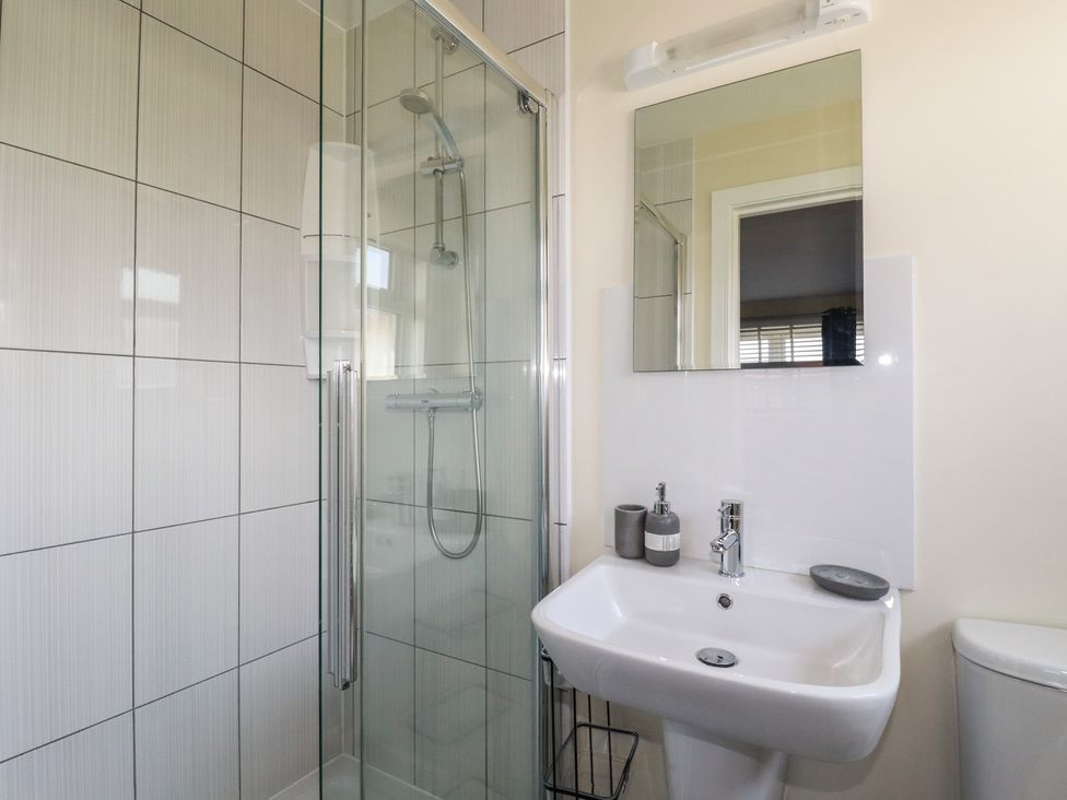 A bathroom with a shower cubicle a sink with soap dispenser and mirror a toilet at Lodge 18 in St Merryn
