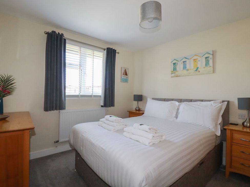 A bedroom with a double bed with white linens two bedside tables with lamps a window with dark curtains and beach themed pictures at Lodge 18 in St Merryn