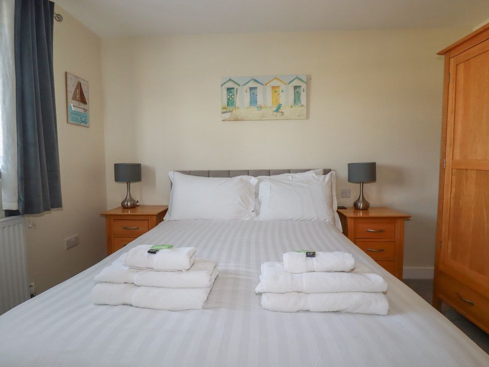 A bedroom with a bed with white linens and stacked towels on top two wooden bedside tables with lamps and a wooden wardrobe at Lodge 18 in St Merryn