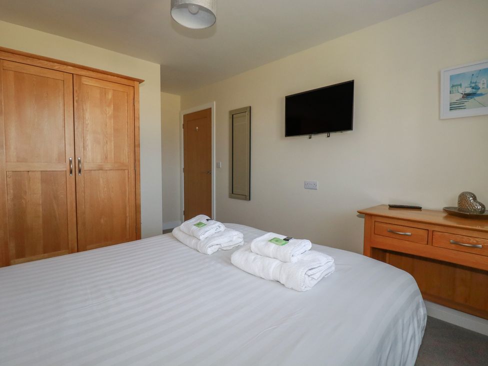 A bedroom with a bed with towels on it a wooden wardrobe a wall-mounted television and a wooden dresser at Lodge 18 in St Merryn