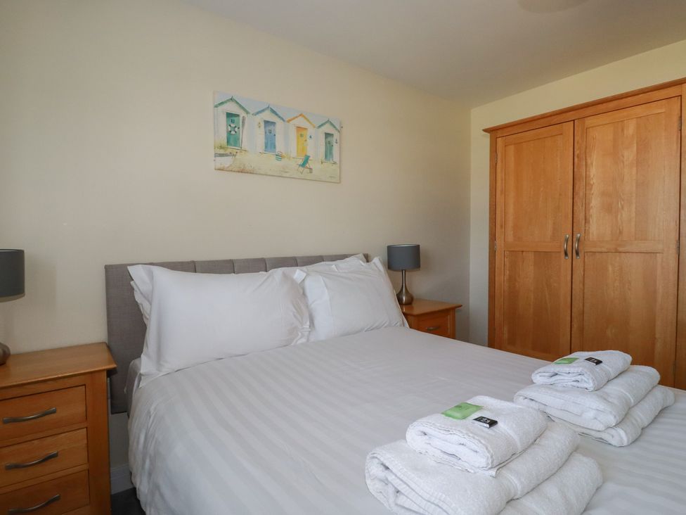A bedroom with a bed with white linens and folded towels bedside tables with lamps and a wooden wardrobe at Lodge 18 in St Merryn