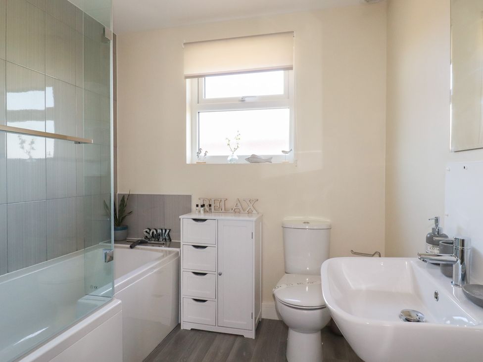 A bathroom with a bathtub and glass shower screen a white cabinet toilet and sink at Lodge 18 in St Merryn