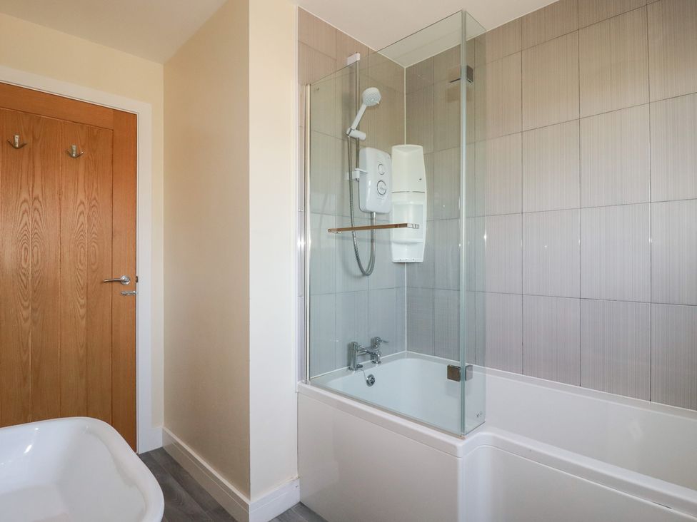 A bathroom with a bathtub shower combination tiled walls glass shower screen and a wooden door at Lodge 18 in St Merryn