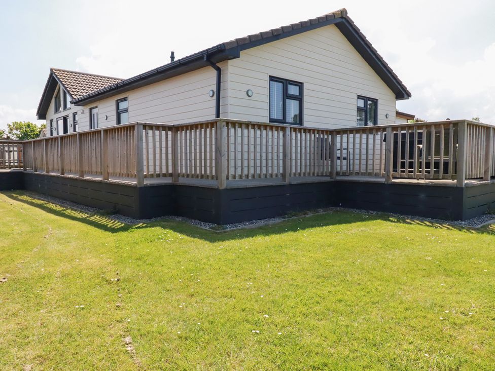 An exterior view of a single-story house with a wooden deck and railing surrounding it at Lodge 18 in St Merryn