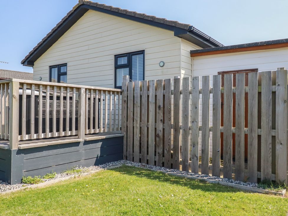 A fenced backyard with a wooden deck attached to a house at Lodge 18 in St Merryn