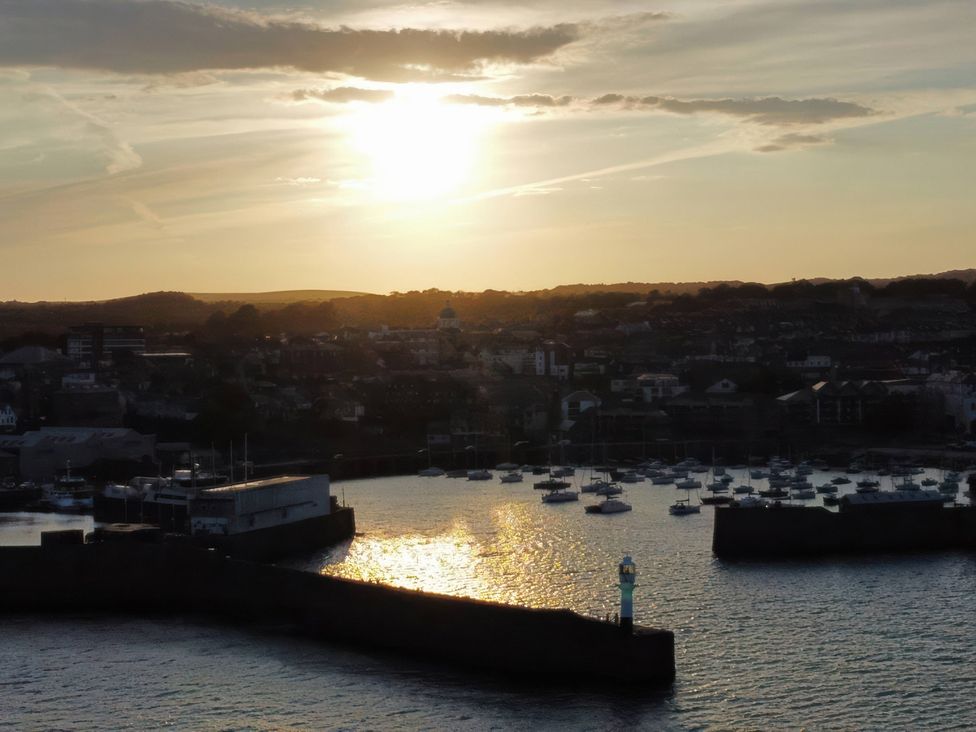 A sunset over a harbor with boats and a lighthouse at Tide Watch in Penzance