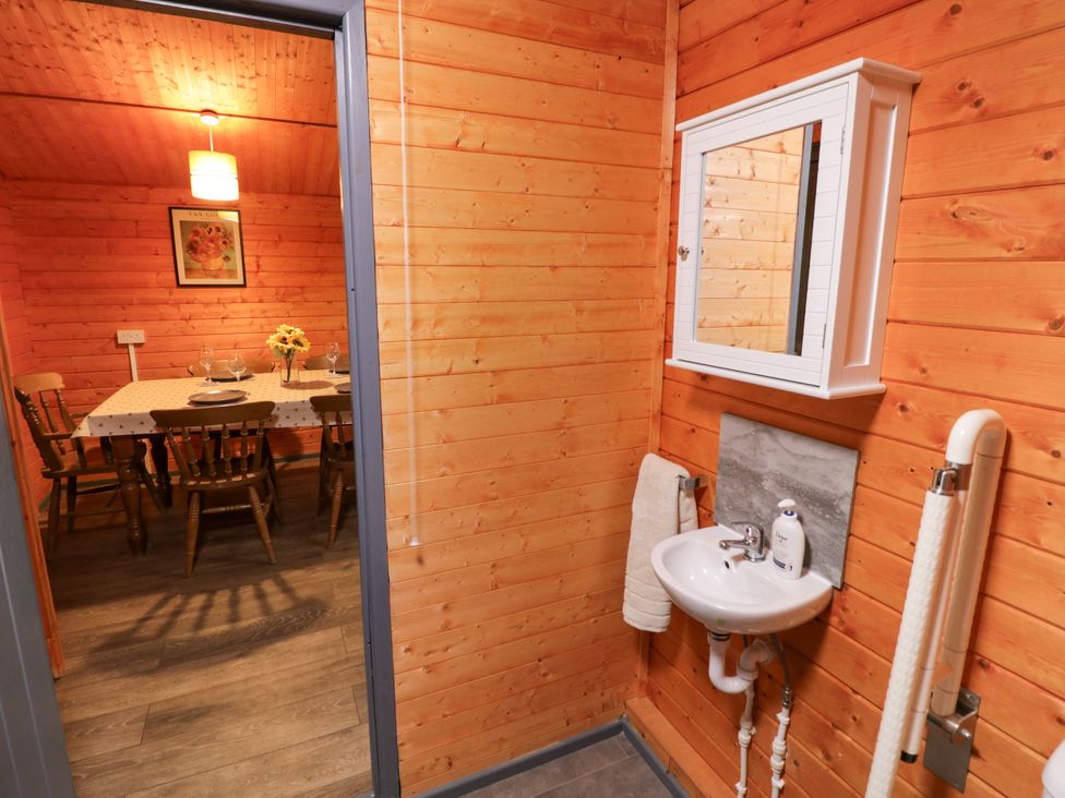 A sink with a mirror in a wooden interior with a dining table at Stumps Cross Lodge Upper Coscombe near Winchcombe