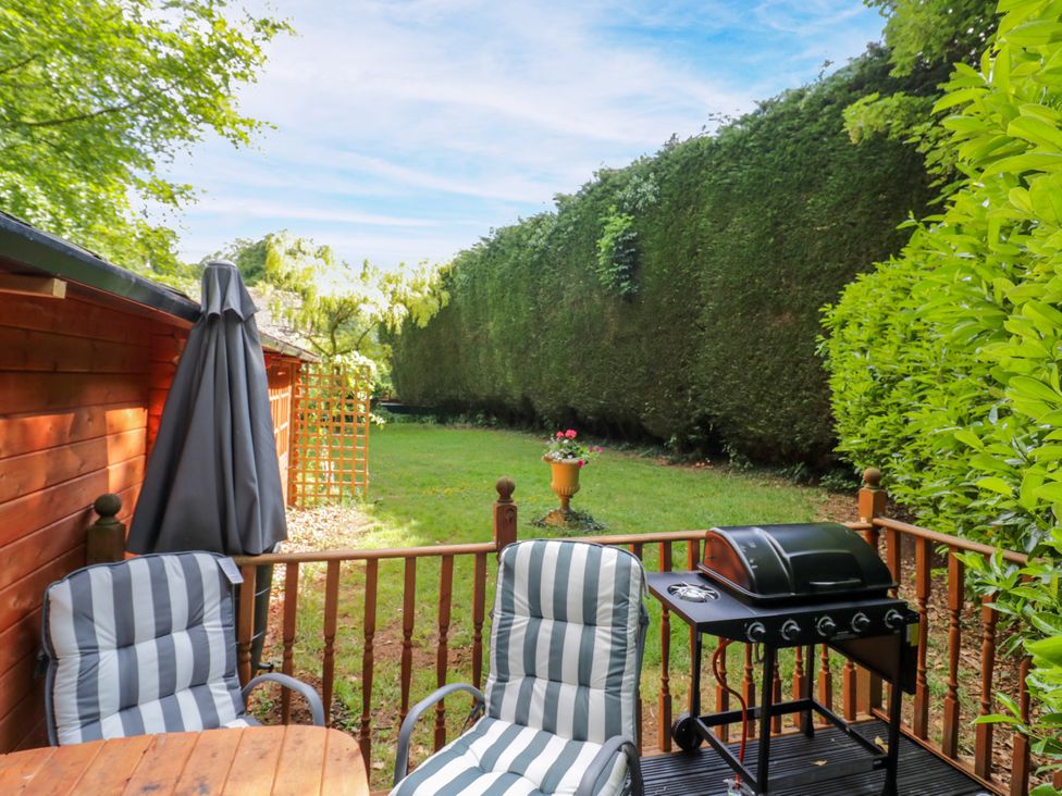 A garden with chairs, table, grill, and a patio umbrella at Stumps Cross Lodge, Upper Coscombe near Winchcombe