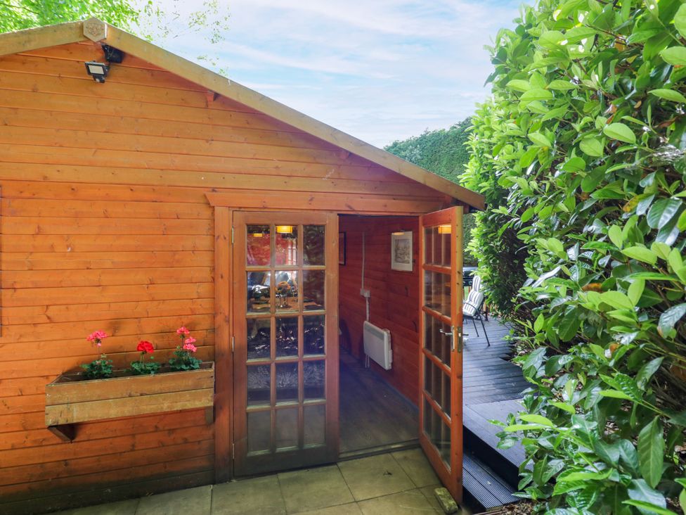 A wooden cabin with a door and flowers in a planter at Stumps Cross Lodge Upper Coscombe near Winchcombe