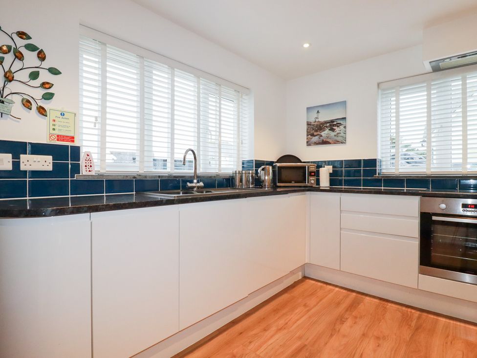 A kitchen with a sink, cabinets, microwave, and oven at Fistral Palms 2