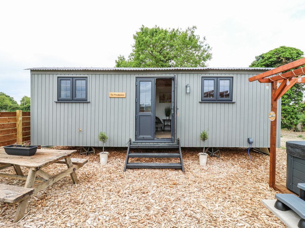 A small grey cabin with a picnic table and hot tub outside at Woodpecker in Lode near Bottisham