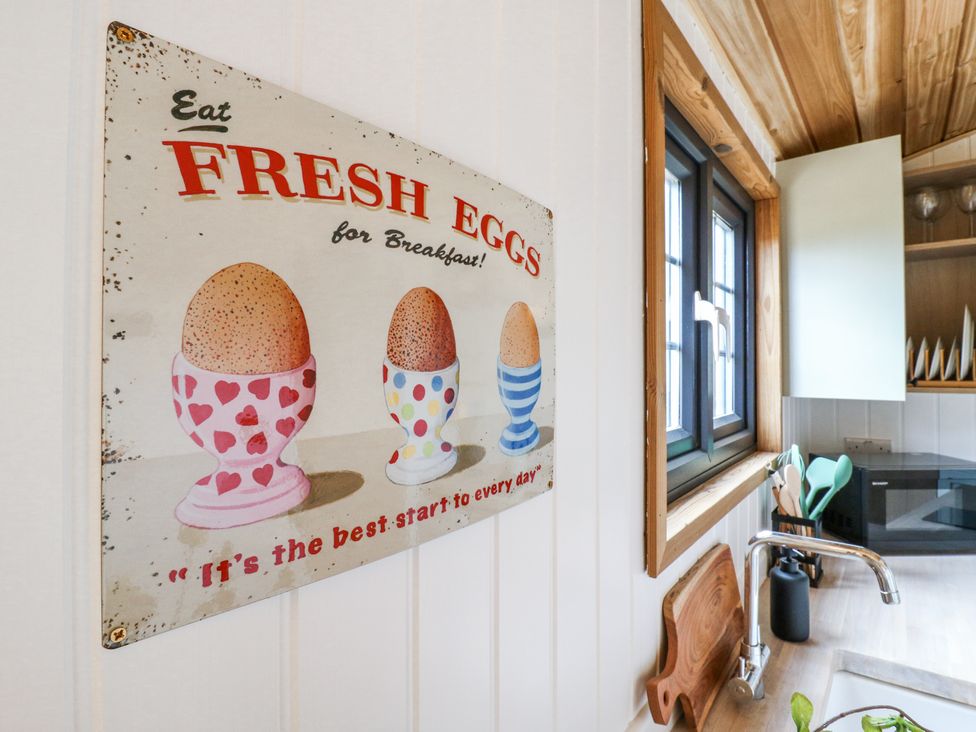 A kitchen wall with a vintage sign about fresh eggs next to a window and a countertop with a faucet and cutting board at Woodpecker Lode near Bottisham
