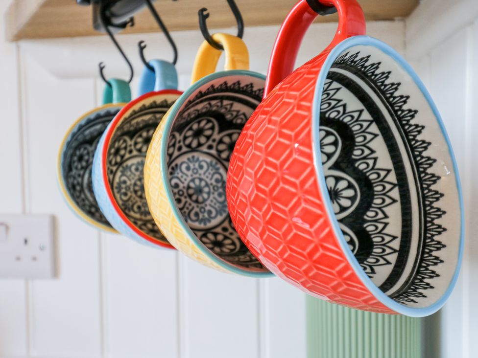 Six colorful ceramic mugs with black and white patterns hanging on hooks in a kitchen at Woodpecker in Lode near Bottisham