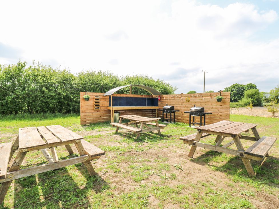 An outdoor area with wooden picnic tables grills and a wooden fence at Woodpecker in Lode near Bottisham