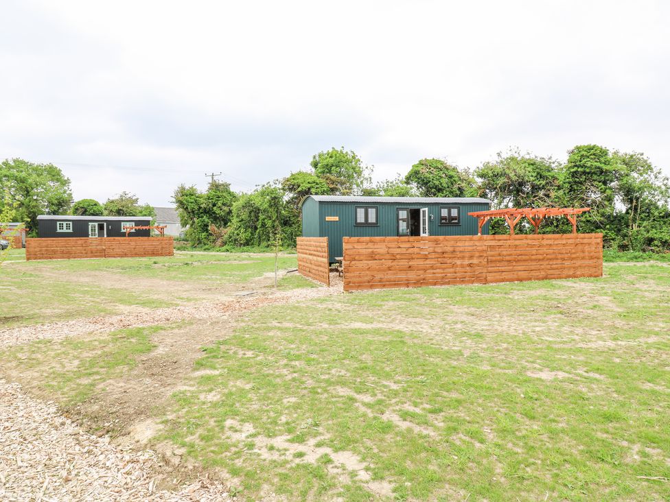 Two small green cabins with wooden fences on a grassy plot with trees in the background at Woodpecker in Lode near Bottisham