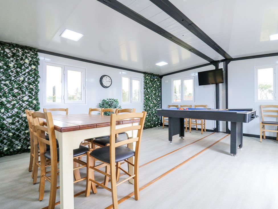 A game room with a pool table wooden chairs and table wall clock and a mounted television at Woodpecker in Lode near Bottisham