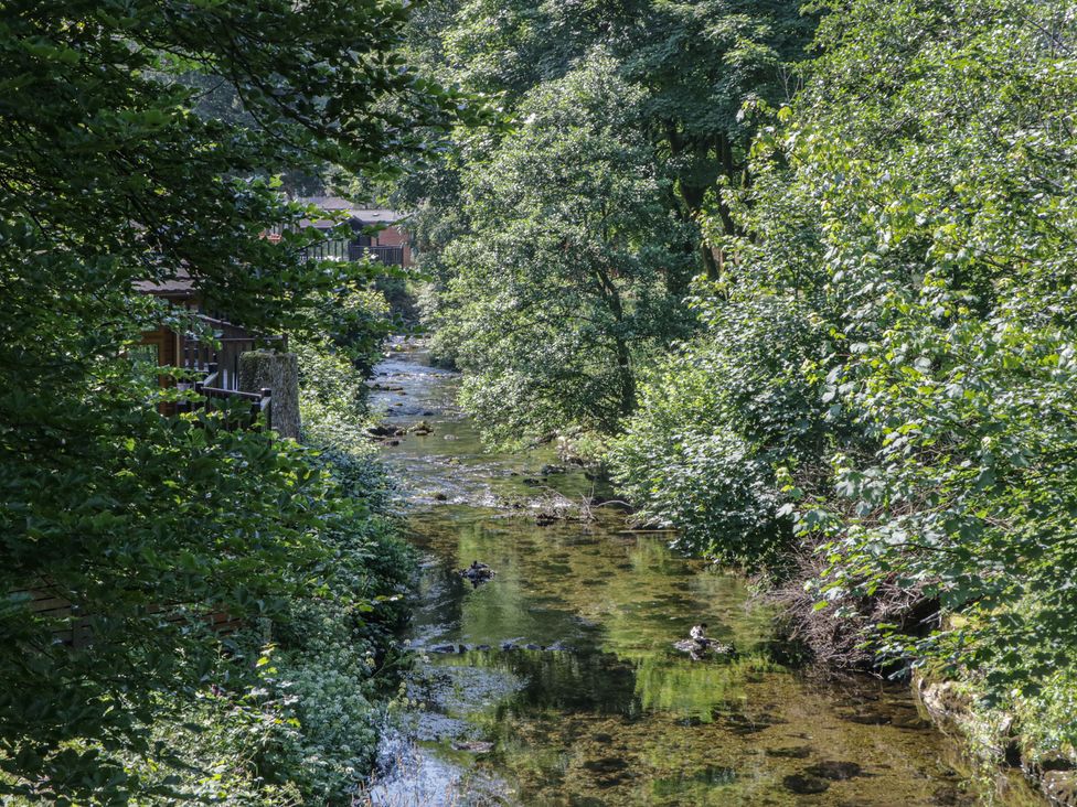 A stream surrounded by trees and buildings at Wally's Folly Limefitt Park near Troutbeck