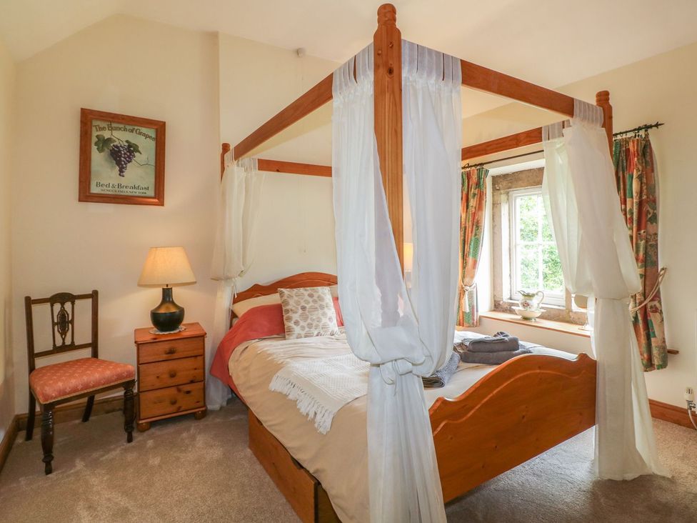 A bedroom with a canopy bed, bedside table, chair, and window at Orchard View in Ashbourne