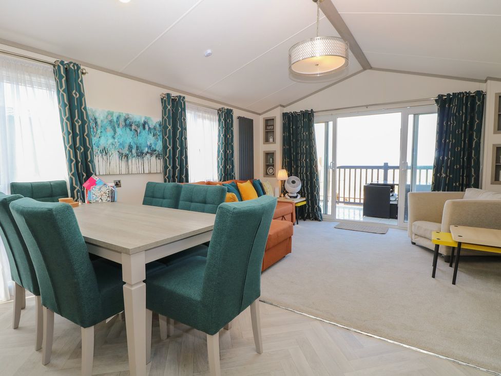 A living room with a dining area and balcony door at Sand & Serenity in Bacton
