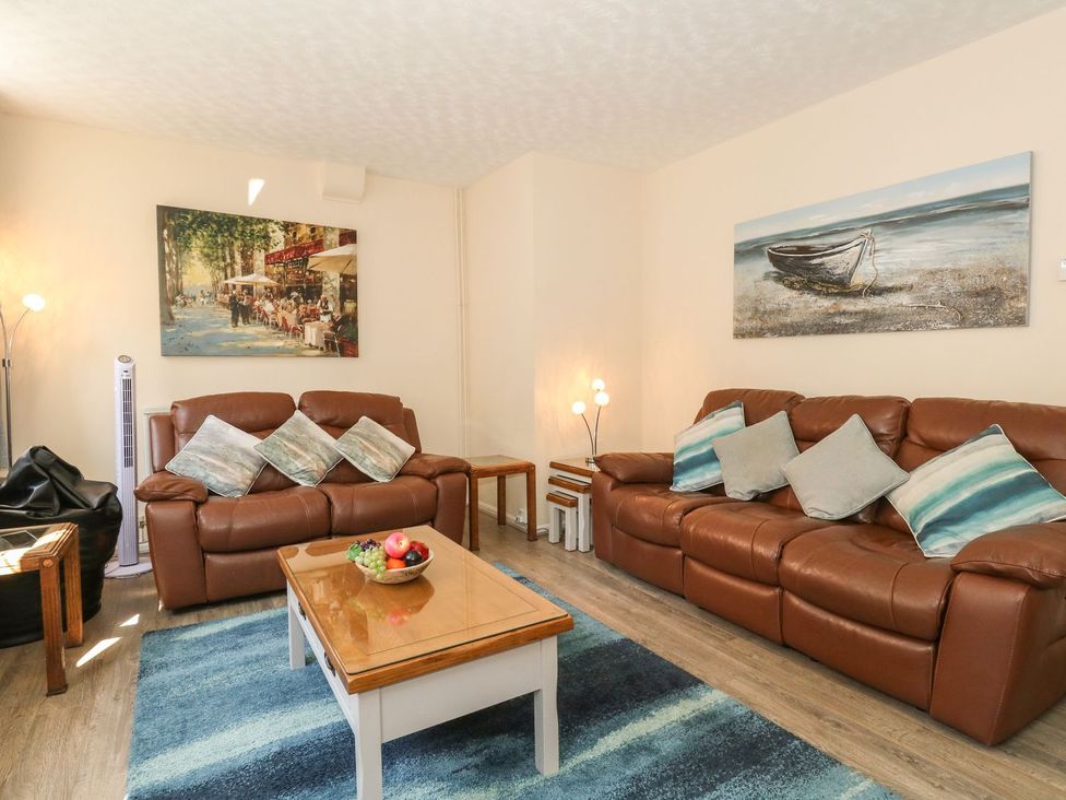 A living room with two brown leather sofas a wooden coffee table with a fruit bowl a blue rug and paintings on white walls at Old Malthouse Apartment in Weymouth
