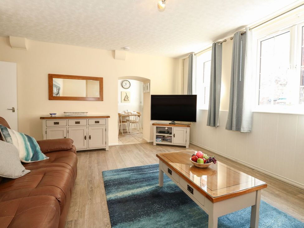 A living room with a brown sofa a coffee table with fruit a television and two light grey cabinets at Old Malthouse Apartment Weymouth