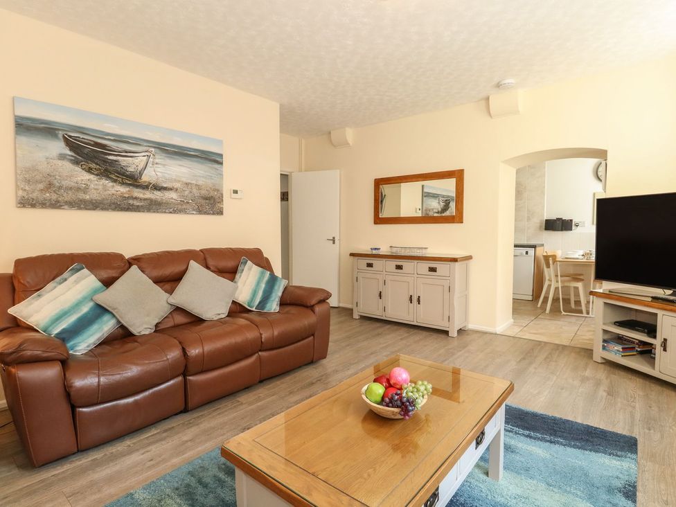 A living room with a brown leather sofa and cushions a wooden coffee table with a bowl of fruit and a television on a stand at Old Malthouse Apartment in Weymouth