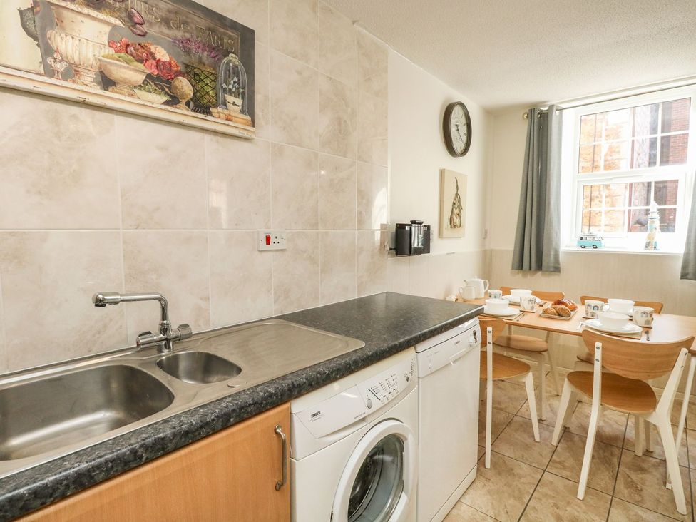 A kitchen with a sink washing machine dishwasher and a dining table set with cups and pastries at Old Malthouse Apartment Weymouth