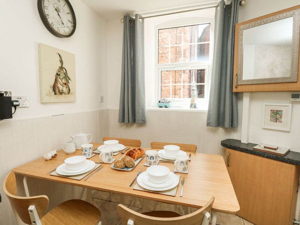 A dining area with a wooden table set for four with plates cups and bread near a window with gray curtains at Old Malthouse Apartment in Weymouth
