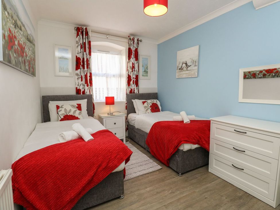 A bedroom with two single beds red blankets and floral curtains at Old Malthouse Apartment Weymouth